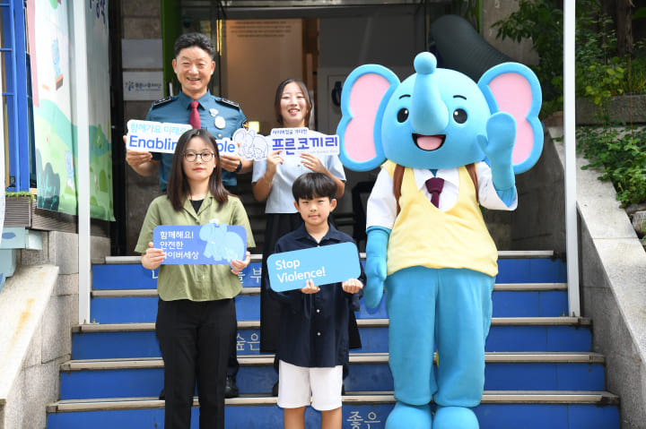 Police officers and children are posing for a photo on the stairs with the Samsung Blue Elephant mascot.