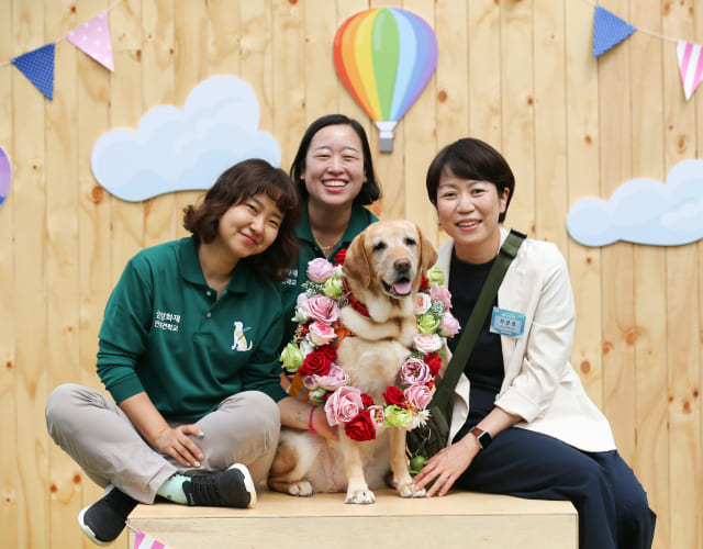 Volunteers who adopted retired senior guide dogs, retired guide dogs, and their trainers are taking a retirement commemorative photo.